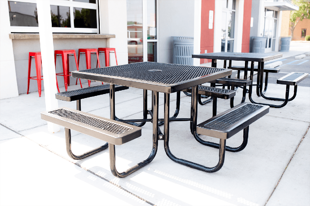 Portable commercial picnic tables with perforated steel tops placed on a restaurant patio, offering flexible outdoor seating for dining and high-traffic environments